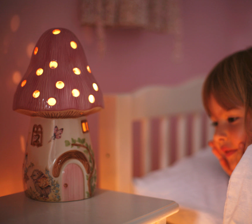 girl in bed with nursery bedside toadstool fairy light in pink glowing onto wall 